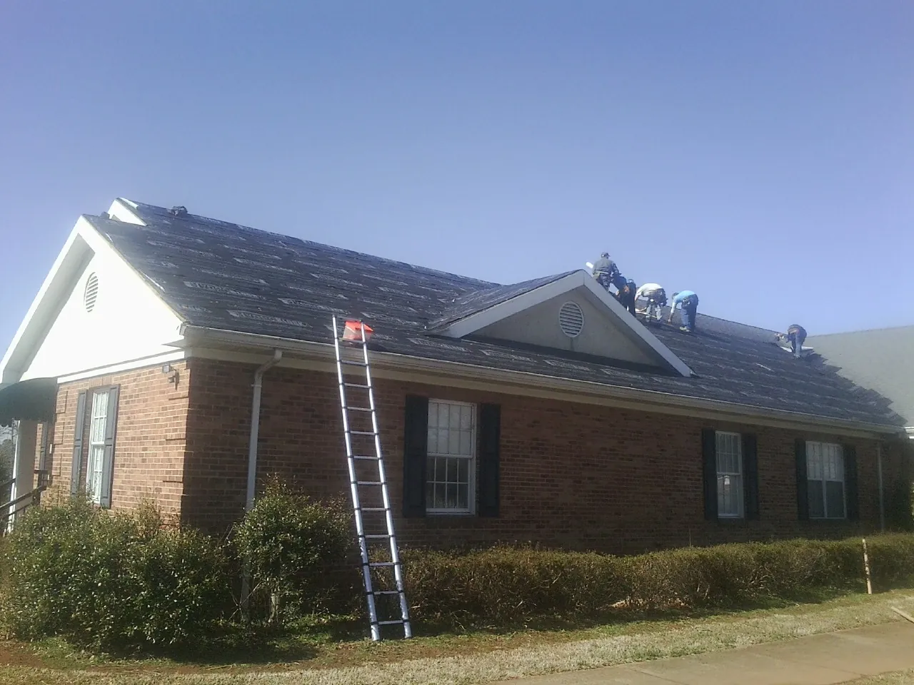 Crew tearing shingles off a brick ranch roof with a ladder set — Metal Roof Repair work by our crew in Nelson