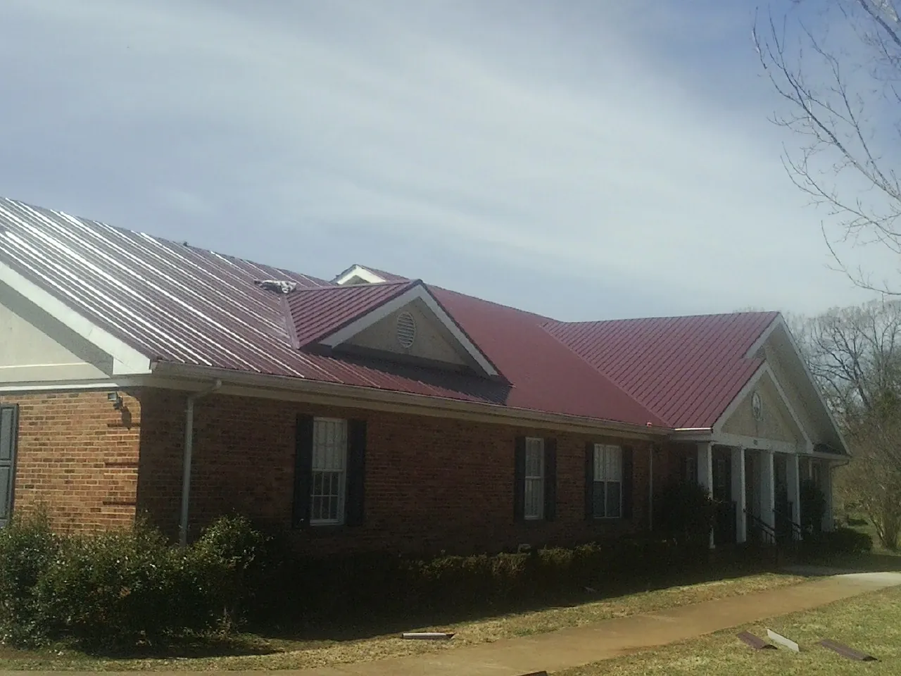 Red metal roof with gabled entries on a long brick building, from a Hail Damage Roof Repair job in Nelson