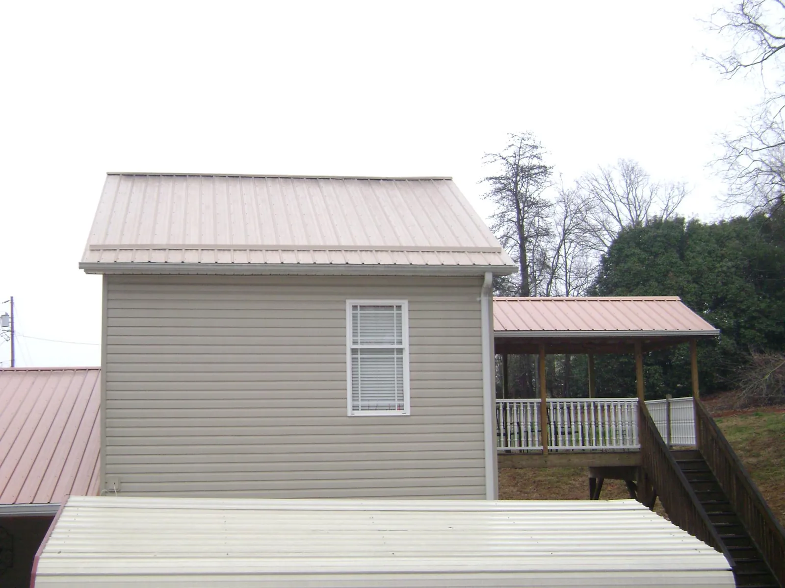 Tan metal roofs on a two story addition and attached porch, from a Roof Replacement job in Nelson